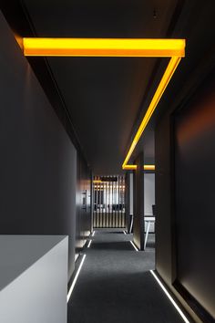 an empty hallway with black walls and yellow lighting on the ceiling is lit by fluorescent lights