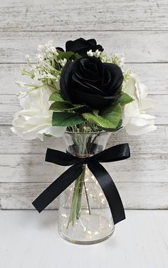 a black rose in a clear vase with white flowers and greenery on the side