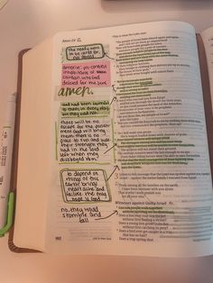 an open bible with green marker writing on it and a pen sitting next to it