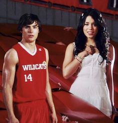 a man and woman standing next to each other in front of a basketball court with red bleachers