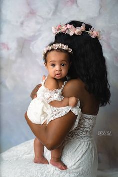 a woman holding a baby in her arms and wearing a flower crown on her head