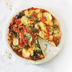 a pizza sitting on top of a white plate covered in cheese and veggies