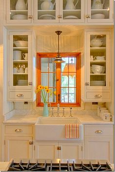 a kitchen with white cabinets and an orange window above the sink in front of it