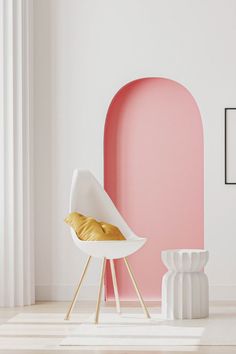 a white chair sitting in front of a pink wall with a gold pillow on it