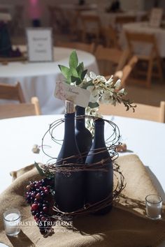 two wine bottles with flowers in them on a table at a wedding or other function