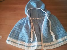 a crocheted blue and white hooded jacket on top of a wooden table