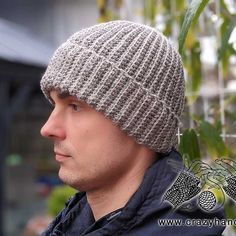 a man wearing a knitted beanie hat in front of a plant with leaves