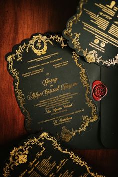 two black and gold wedding cards with red wax stamp on them, sitting next to each other