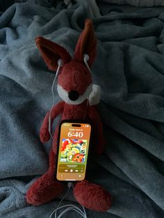 a red stuffed animal laying on top of a bed next to a cell phone charger