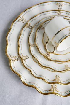 four white and gold plates stacked on top of each other with a cup in the middle