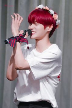 a woman with red hair holding a microphone and wearing a flower crown on her head