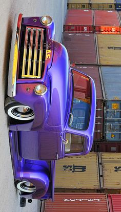 a purple car is parked next to some shipping containers on the side of a road