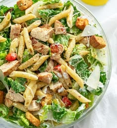 a salad with chicken, lettuce and tomatoes in a glass bowl on a white table