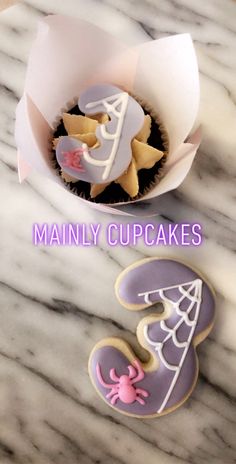 two decorated cookies sitting on top of a table next to a cupcake in the shape of a number