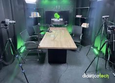 an office with green lighting and camera equipment in front of a desk that is surrounded by black chairs