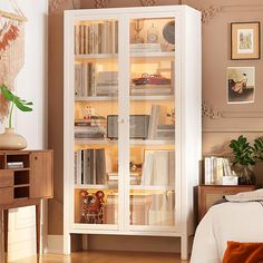 a white bookcase with many books on it in a bedroom next to a bed