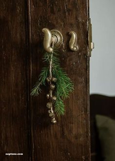 a door handle with bells hanging from it's side and a pine branch on the other side