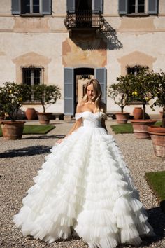 a woman standing in front of a building wearing a wedding dress with ruffles