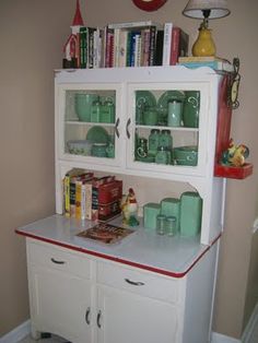 a white china cabinet with glass doors and red trim on the bottom, sitting next to a wall mounted clock