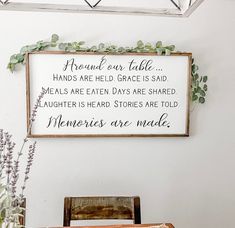 a wooden sign hanging on the wall above a table with flowers and other items in front of it