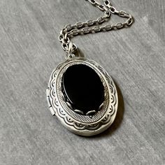 Antique Silver Onyx Locket Necklace....  This locket necklace is beautiful!  The locket is made of brass and is antique silver plated.  To the center of the locket, I added a flat top oval black onyx cabochon that sits in an antiqued silver brass setting. The high quality chain has soldered links and is non tarnish.  The chain closes with a lobster claw clasp.         Locket - 29mm height x 22mm width approximately Interior photo area - 20mm x 15mm wide approximately Chain - 24 inches long This sweet vintage style locket would be perfect to add photos of relatives, friends or pets. Your locket necklace will come to you gift wrapped!   More beautiful lockets!  https://www.etsy.com/shop/dayslonggone/?etsrc=sdt&section_id=6107145 Nature and vintage inspired necklaces!  https://www.etsy.com/sh Black Medallion With Large Pendant, Black Sterling Silver Locket Necklace, Black Oval Pendant Necklace With Spiritual Style, Black Oval Pendant Necklace Spiritual Style, Black Oxidized Medallion Jewelry, Black Bohemian Medallion Jewelry, Black Round Locket Necklace, Vintage Oval Necklace With Oxidized Finish, Black Round Pendant Necklace For Memorial