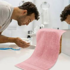 a man cleaning his face with a pink towel in the bathroom while another man looks on