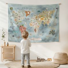 a little boy standing in front of a wall hanging with a map of the world on it