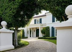 a large white house with green shutters on the front and side doors, surrounded by trees