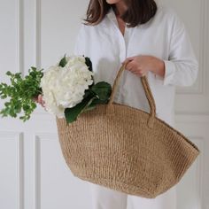 a woman is holding a basket with flowers in it and she is wearing white pants