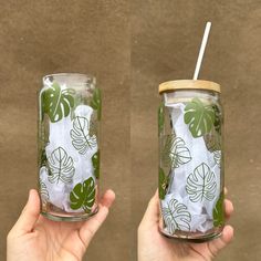 two people holding up mason jars with green leaves on them, one is empty and the other has a straw in it