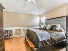 a bedroom with a bed, dresser and chair next to a wall mounted tv in the corner