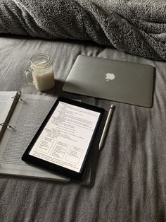 an open book, pen and laptop on a bed with a glass of milk next to it