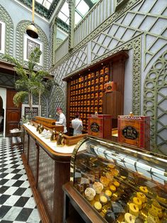 two men are standing at the front counter of a pastry shop with pastries on display