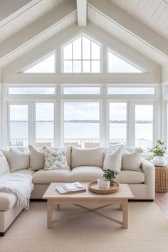 a living room filled with white furniture and large windows overlooking the water on a sunny day