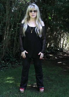 a woman standing in the grass with her hands on her hips wearing sunglasses and black clothing