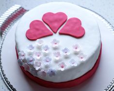 a cake with white frosting and pink hearts on top, sitting on a plate