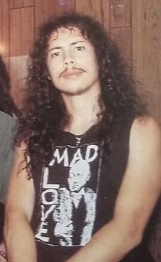 two men sitting next to each other in front of a wood paneled wall, one with long curly hair