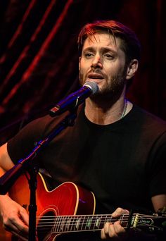 a man holding a guitar while standing in front of a microphone and singing into a microphone