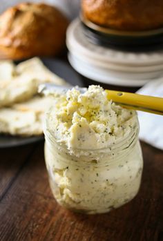 a jar filled with cream cheese sitting on top of a wooden table next to muffins