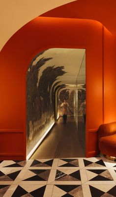 an orange hallway with black and white tiles on the floor, along with a person walking down it