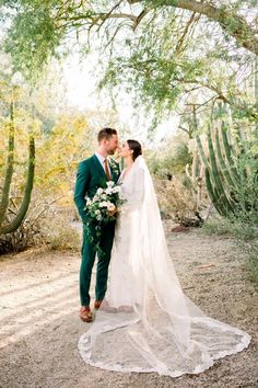 a bride and groom standing in front of cactus trees