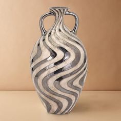 a silver and black vase sitting on top of a table next to a brown wall