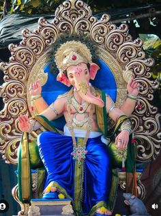 an elephant statue sitting on top of a blue and gold chair in front of a tree