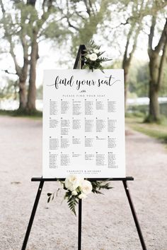 a sign with flowers and greenery on it in the middle of a dirt road