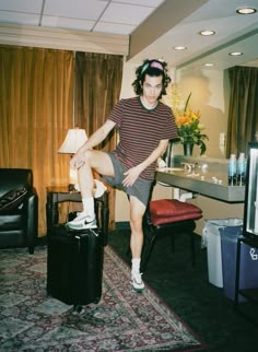 a woman sitting on top of a piece of luggage in a living room next to a table