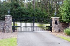 an iron gate with stone pillars and gates leading to a driveway in front of some trees