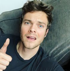 a man laying on top of a couch giving the thumbs up sign with his right hand