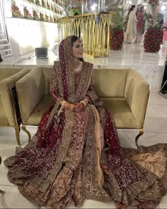 a woman sitting on top of a couch wearing a red and gold wedding dress,