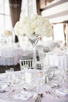 a tall vase filled with white flowers sitting on top of a table covered in silverware