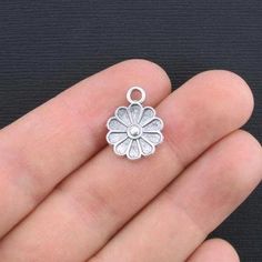 a small silver flower charm on someone's hand with it's thumb in the middle